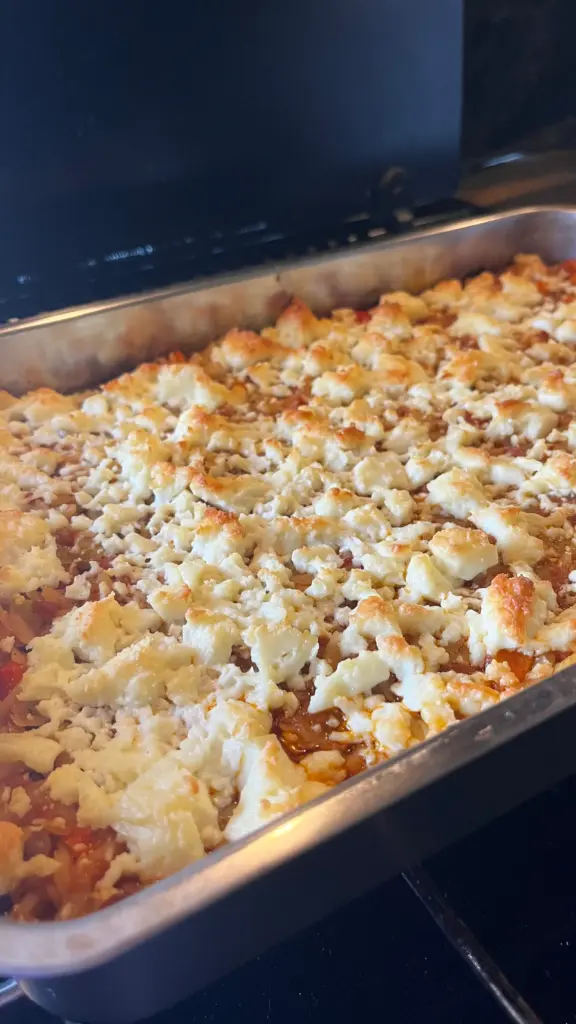 überbackener Kritharaki Auflauf in einer Form mit knusprig goldbraunem Feta